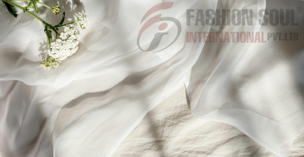 A close-up of white fabric with delicate white flowers and green stems resting on it, with a semi-transparent logo of 