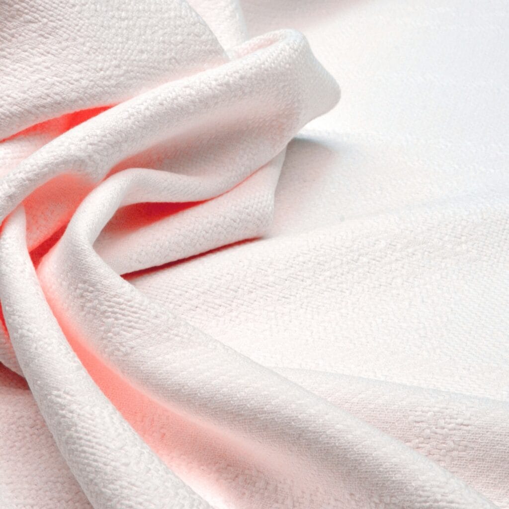 Close-up image of a piece of white long-staple cotton fabric with a soft and smooth texture, gently gathered with some light pink fabric underneath.