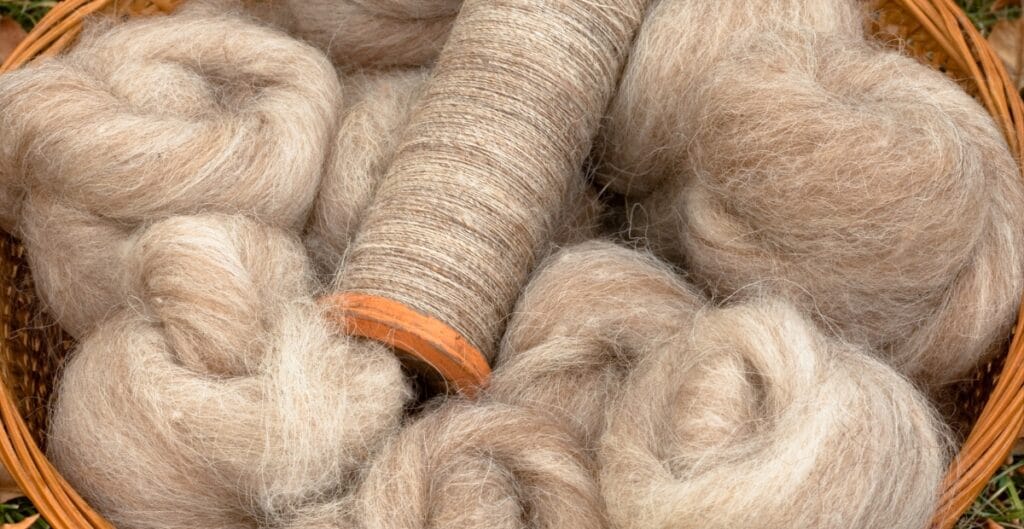 A basket containing natural fibers, including several balls of soft wool and a spool of twine, displayed together.