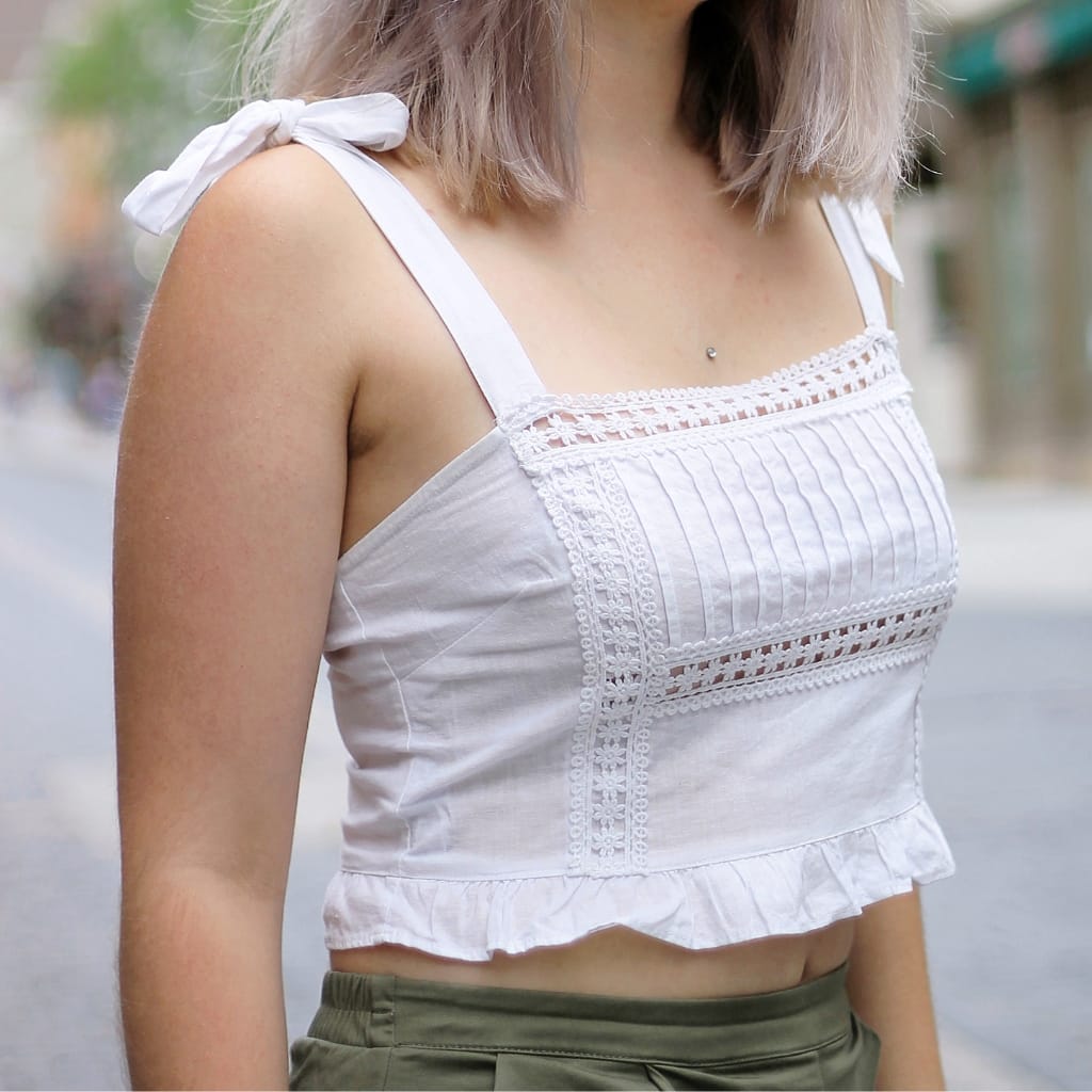 Close-up image of a woman wearing a white sleeveless cropped active top with decorative lace and ruffled hem, made from a lightweight, breathable fabric.