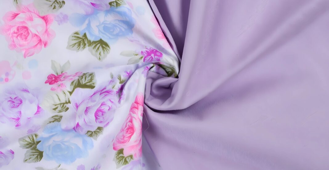 Close-up photograph of fabric with floral print on one side and plain purple fabric on the other, slightly gathered in the