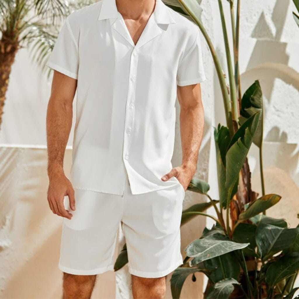 Man wearing a crisp white short-sleeve vacation shirt standing next to lush green plants on a sunny terrace.