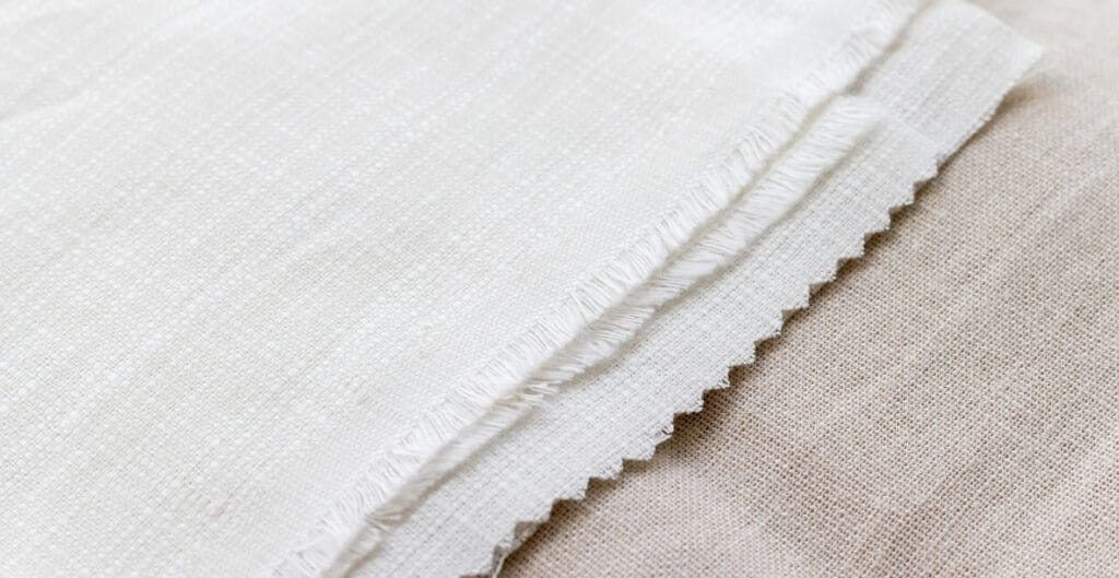 Close-up of a piece of plain weave cotton fabric, showing the tight, evenly woven texture and frayed edge.