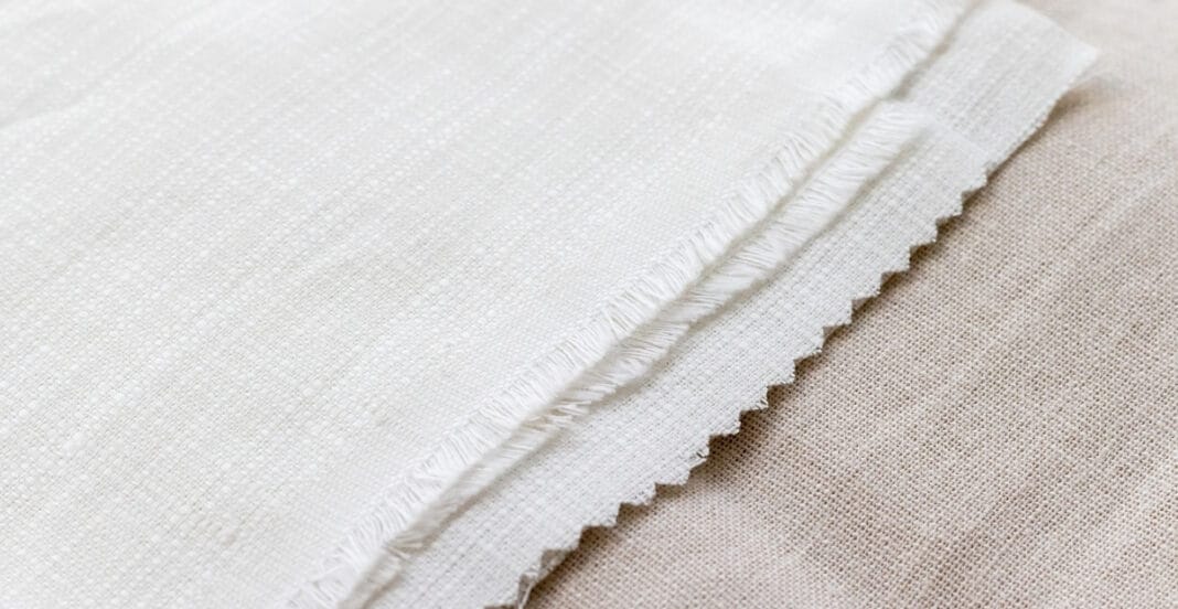 Close-up of a piece of plain weave cotton fabric, showing the tight, evenly woven texture and frayed edge.