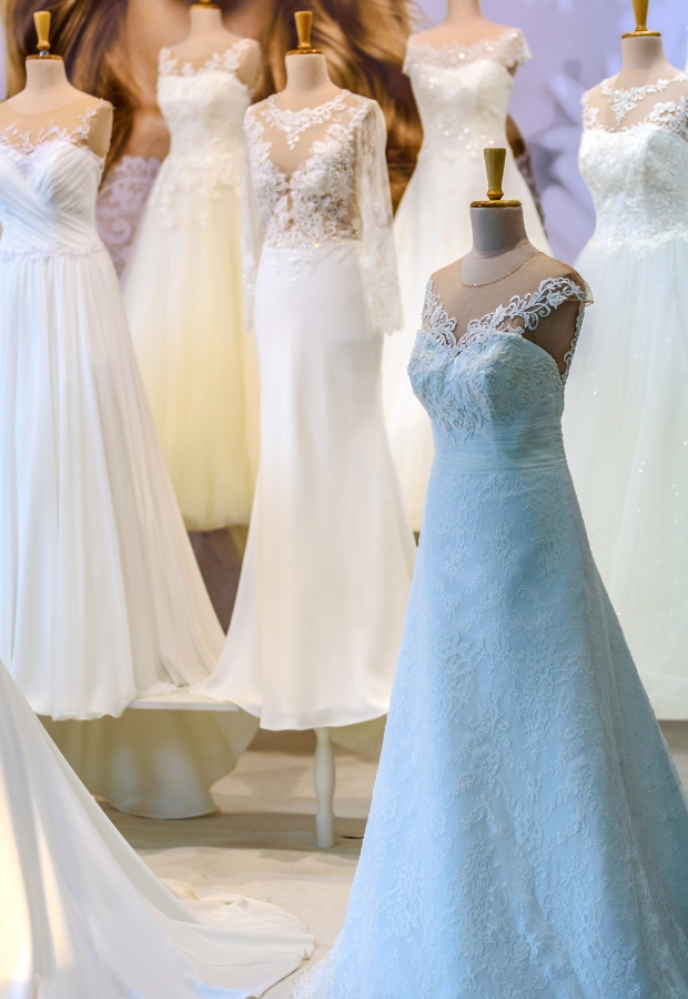 A display of elegant prom dresses on mannequins, featuring various styles in white and ivory, with lace, chiffon, and satin fabrics, set against a softly lit background.