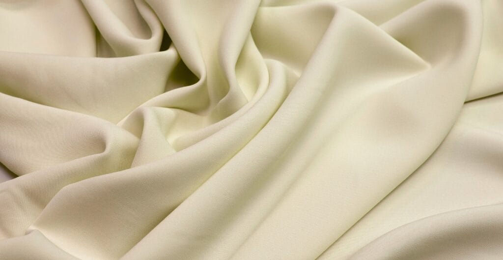 Close-up image of soft, cream-colored rayon spandex fabric with gentle folds.