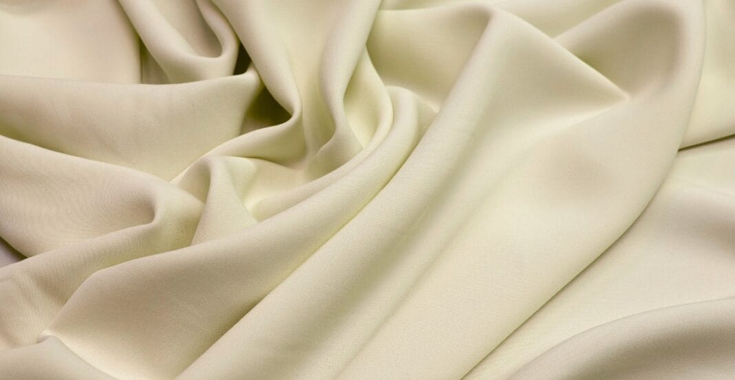 Close-up image of soft, cream-colored rayon spandex fabric with gentle folds.