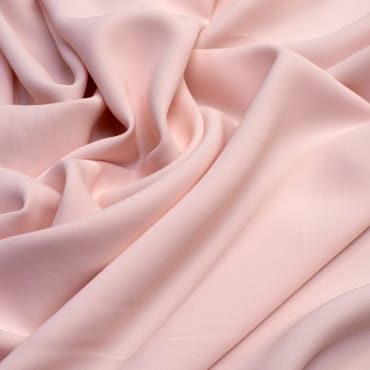 Close-up image of soft, pale pink rayon-spandex fabric with gentle folds and smooth texture.