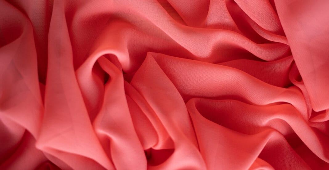 Close-up image of pink rayon chiffon fabric, showing soft, flowing folds and a slightly translucent, textured surface.