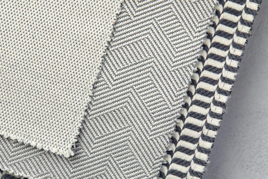 Close-up image of layered textured fabrics featuring different weaving patterns, including herringbone and striped designs, in neutral tones.