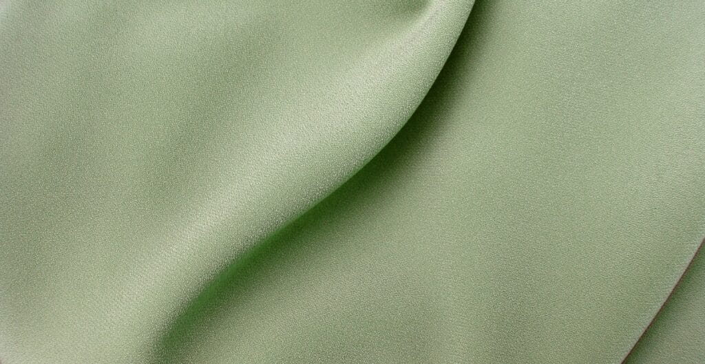 Close-up image of smooth, soft, light green fabric with subtle sheen and gentle folds, showcasing the texture of Tencel fabric.