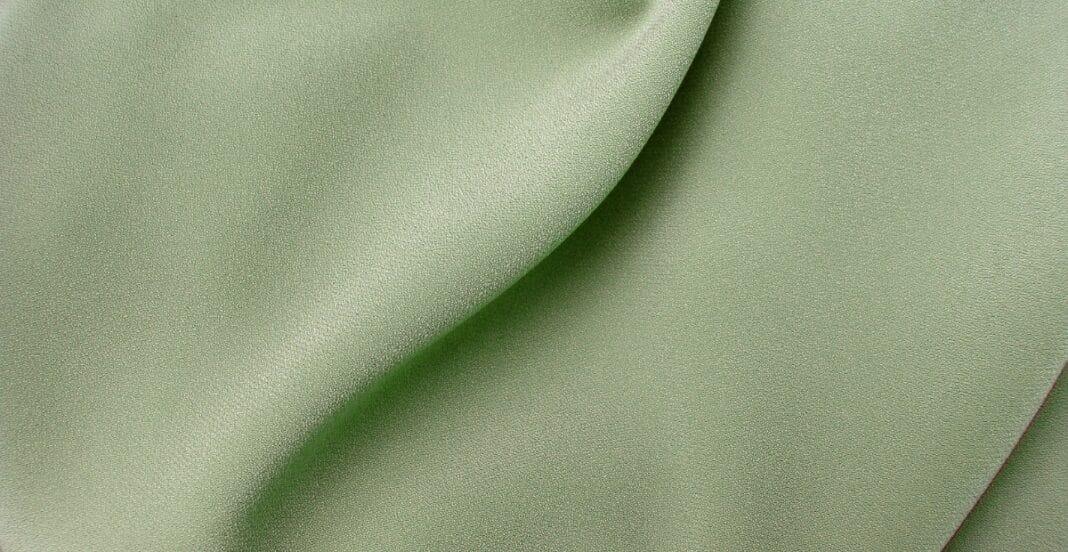 Close-up image of smooth, soft, light green fabric with subtle sheen and gentle folds, showcasing the texture of Tencel fabric.