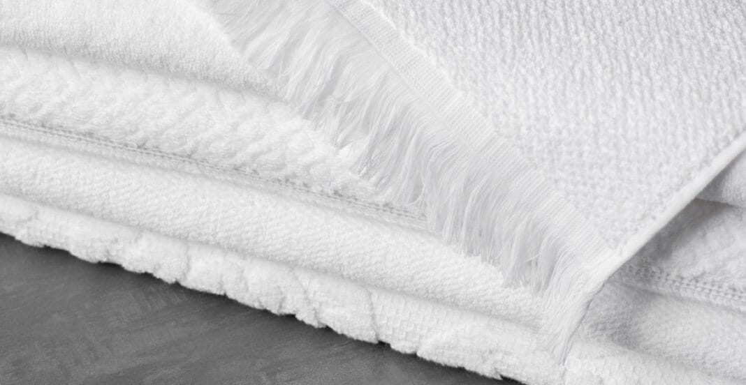 Close-up of thick white cotton fabric with a textured surface and fringed edges, folded over a grey surface.
