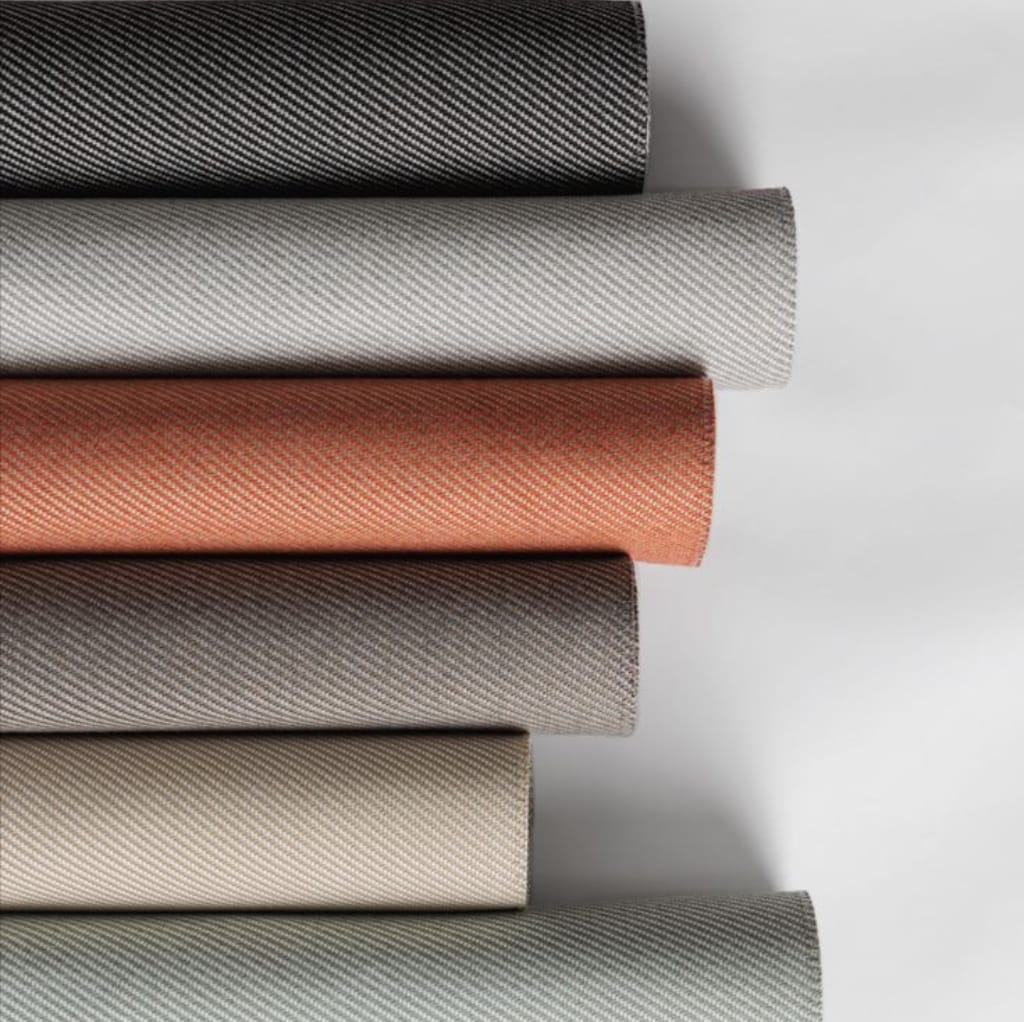 A stack of various twill weave cotton fabrics in different colors, including black, white, rust, beige, and gray, each showcasing a diagonal twill pattern.