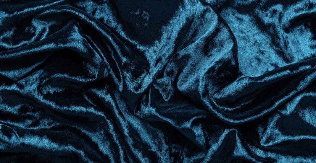 A close-up image of rich, dark blue velvet fabric with a soft, plush texture and subtle sheen.