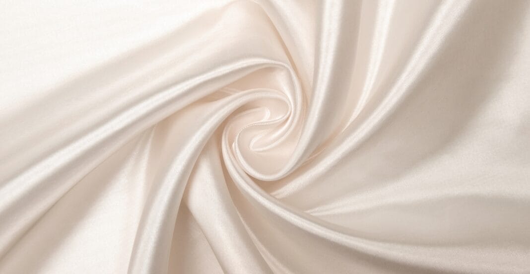 Close-up view of smooth, cream-colored silk organza fabric with a swirling pattern.