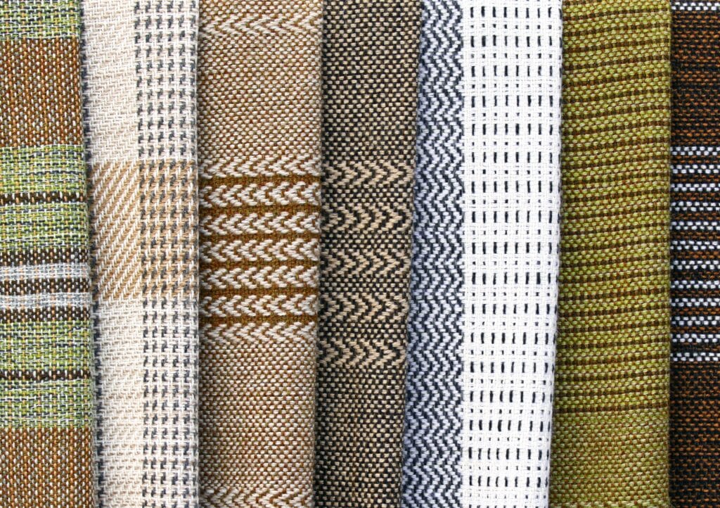 Close-up image of a variety of cotton weave fabrics with different patterns and colors, including checkered, striped, zigzag, grid, and textured designs.