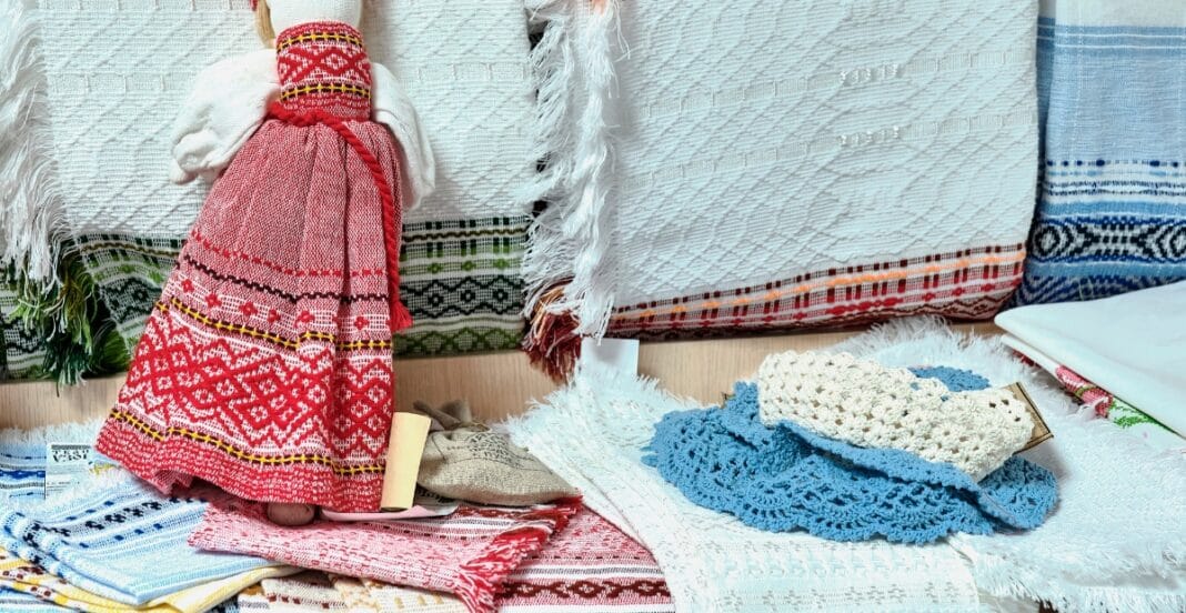 A display of traditional woven textiles, including a doll dressed in a red patterned woven dress, along with various other pieces of woven fabric in different colors and weaves.