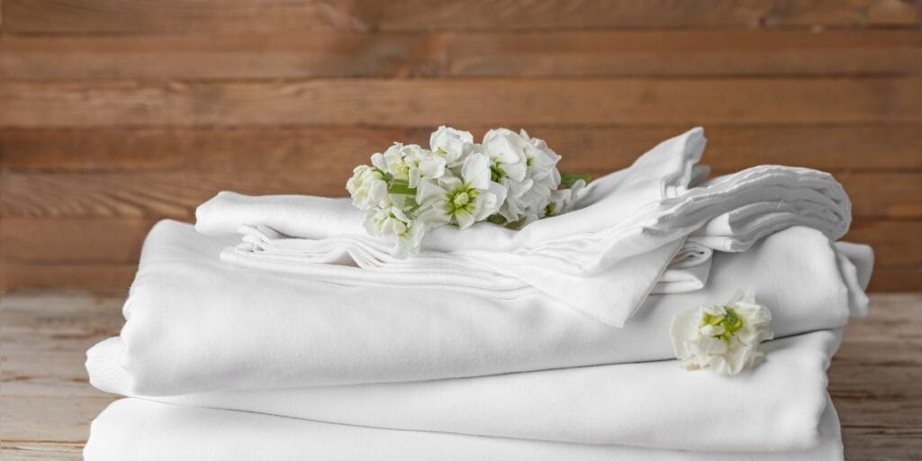 A neatly arranged stack of white towels with white flowers on top, set against a wooden background.