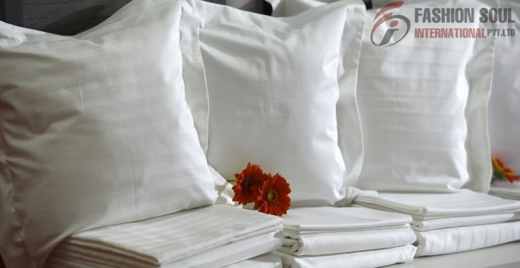 A neatly arranged set of white satin pillowcases and bedsheets with a small orange flower placed between them, on a bed or display surface.