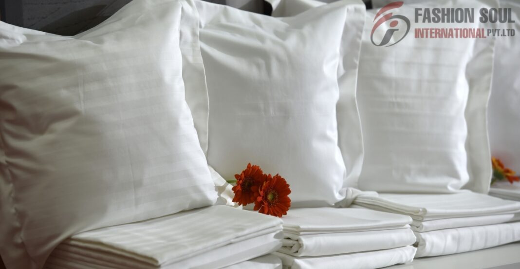A neatly arranged set of white satin pillowcases and bedsheets with a small orange flower placed between them, on a bed or display surface.