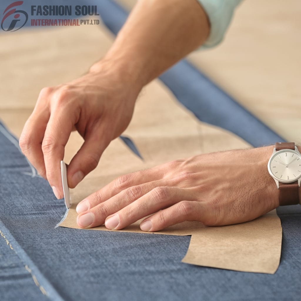 Close-up of a designer cutting fabric using a paper pattern on denim material for precise tailoring.