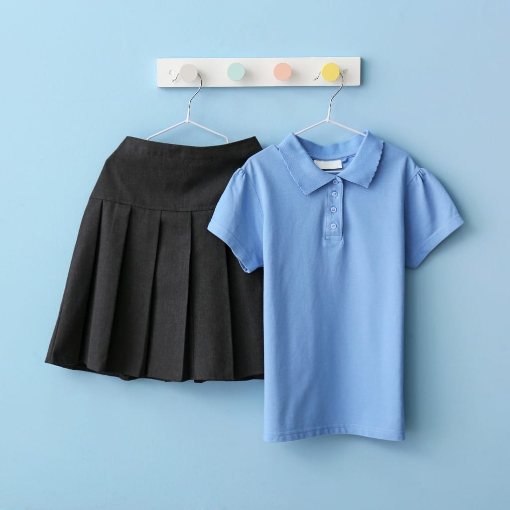 The image shows a blue polo shirt and a black pleated skirt hanging on a pastel-colored wall with a coat rack that has four pastel-colored hooks.