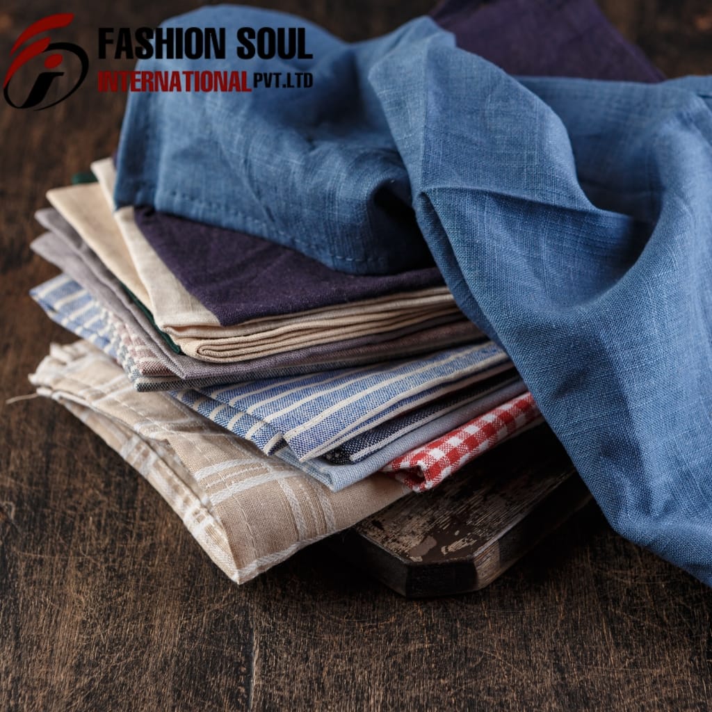 A neatly stacked pile of various fabric swatches, including plaid, striped, and solid colors, placed on a dark wooden surface.