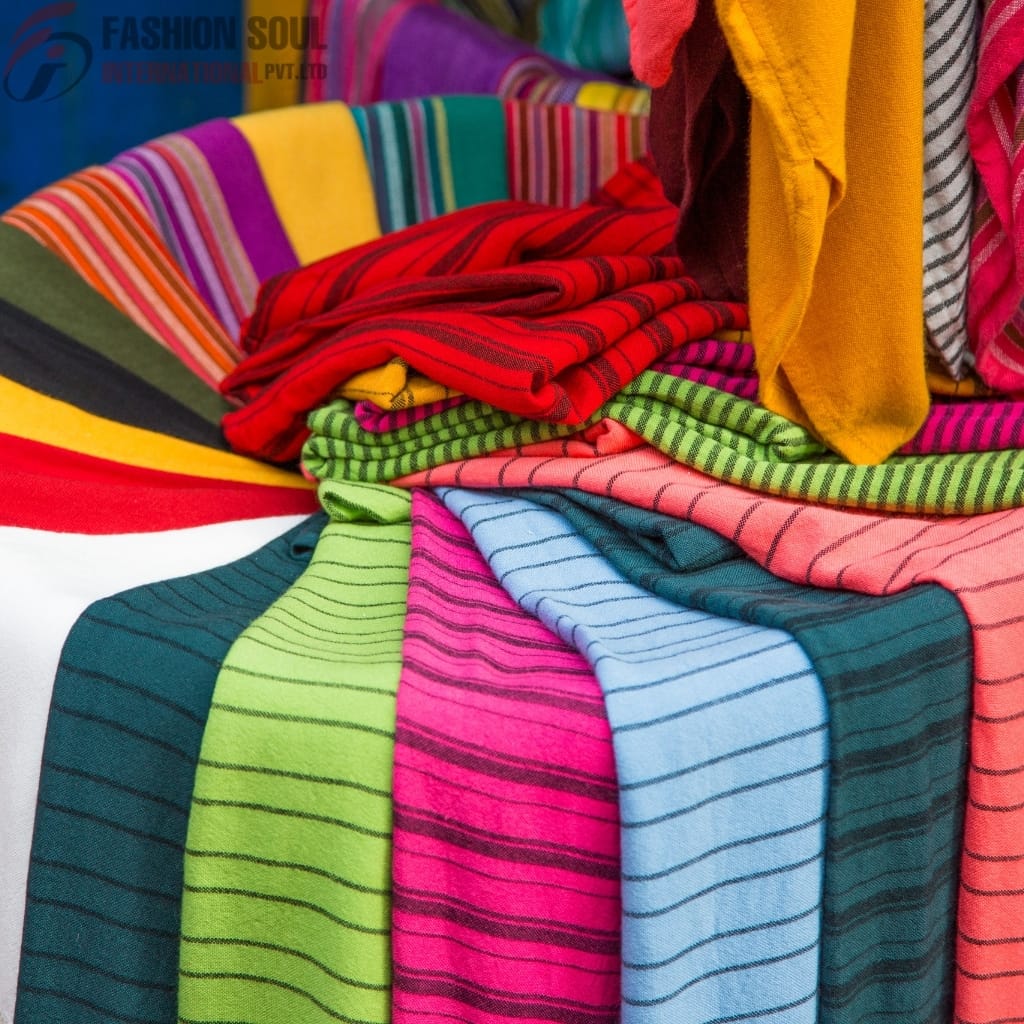 A colorful display of folded fabric and clothing with various bright stripes and patterns, including yellow, red, pink, green, blue, and black.