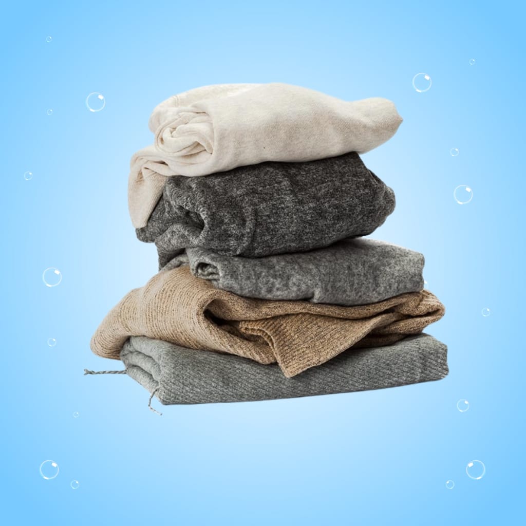 A neatly folded stack of six variously colored sweaters against a light blue background with small bubbles.
