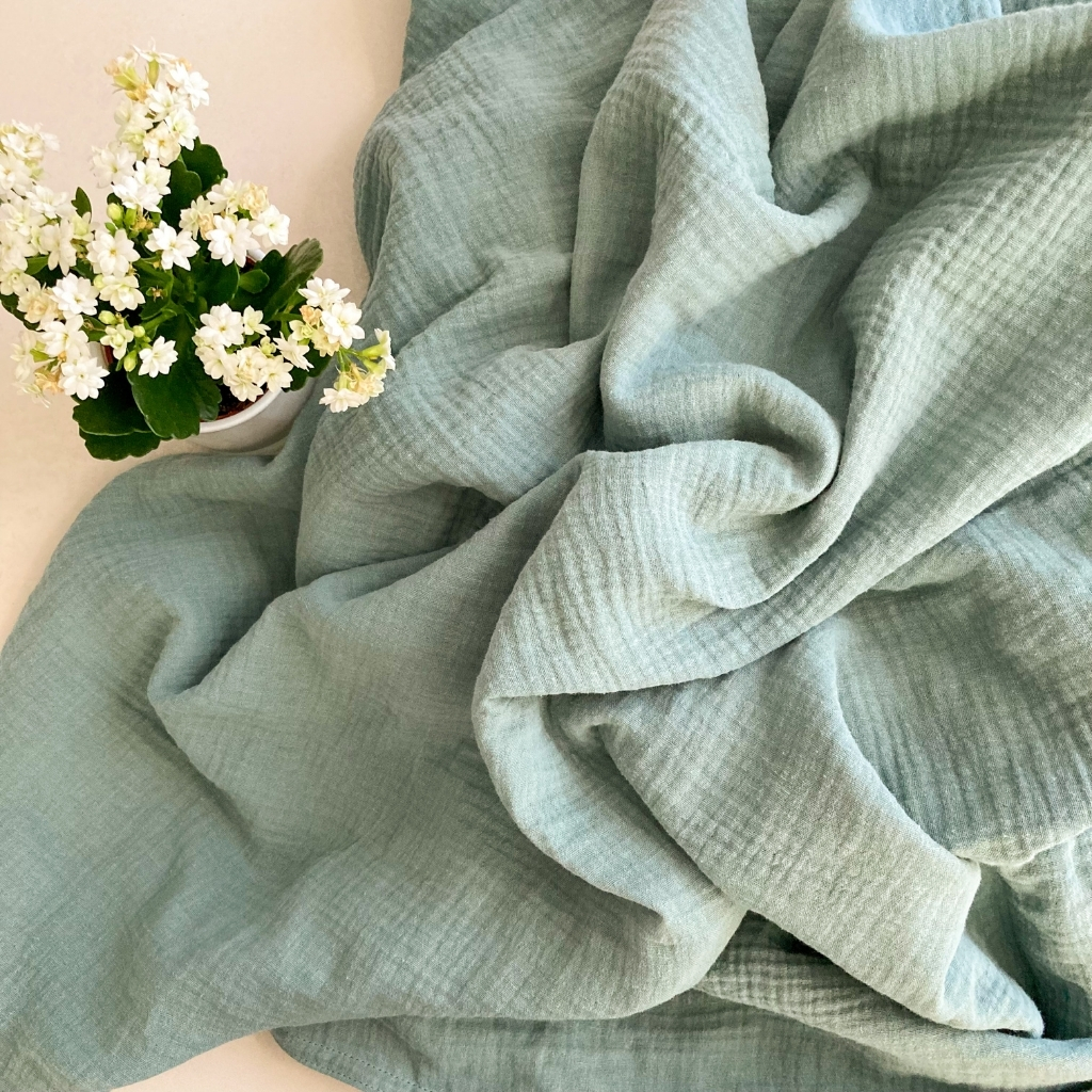 Soft, light green fabric with a checked texture, draped in gentle folds next to a white pot of small white flowers.