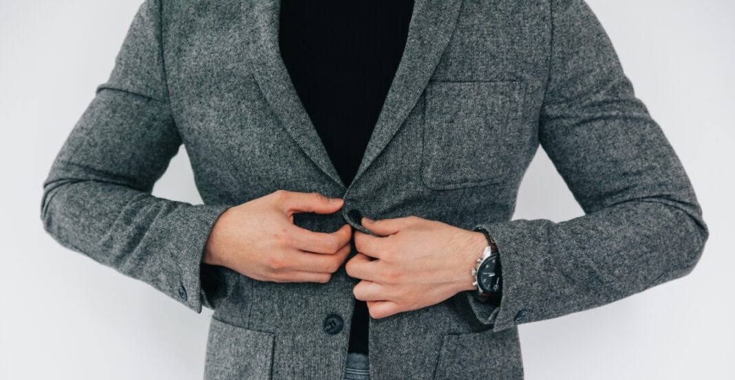 A person adjusting a grey sport coat, wearing a black shirt and a black wristwatch.