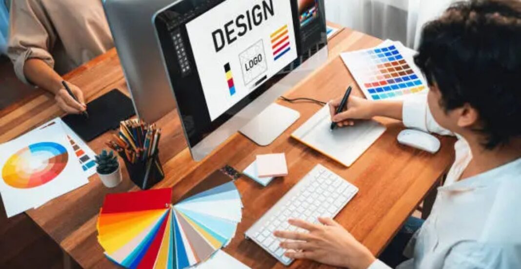Graphic designers working at a desk with color palettes and a computer screen displaying the word 