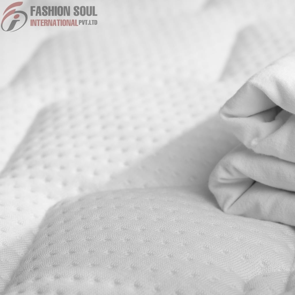  Close-up of a person wearing a white glove touching a textured white fabric, possibly bedding or mattress cover, with a subtle dotted pattern.