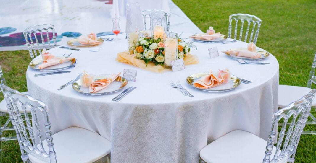 Elegant round table with inexpensive white table linens, floral centerpiece, candles, and neatly arranged place settings.