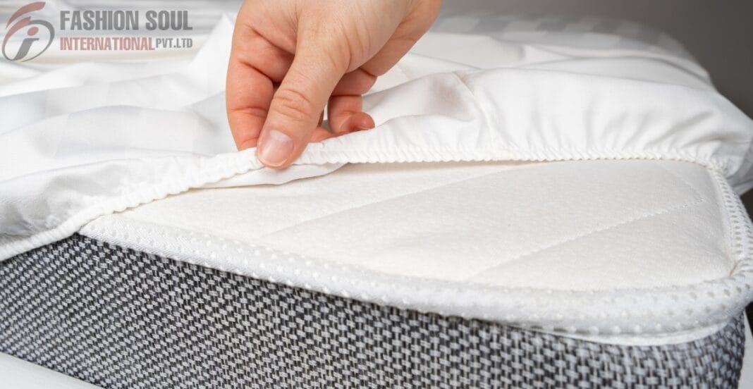 A hand lifting the white mattress cover to reveal a cushioned mattress inside a checkered fabric bed base.