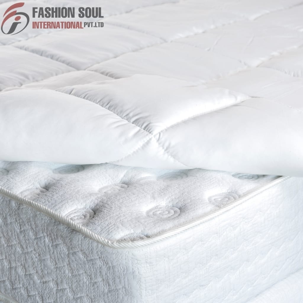 A close-up of a neatly made bed with a white quilted mattress and a white quilted duvet, featuring the "Fashion Soul International Pvt. Ltd" logo in the top left corner.