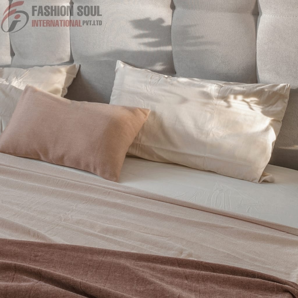 A neatly made bed with beige and cream-colored bedding, featuring two large pillows and a smaller velvety pillow in front, against a soft gray upholstered headboard.