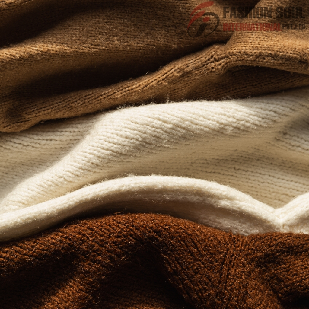 Close-up photo of three folded knitted sweaters in shades of brown and cream, arranged in layers.