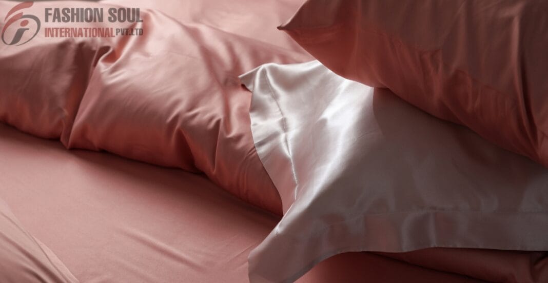 A close-up of a bed with pink satin sheets and matching pillowcases, shown in soft lighting.