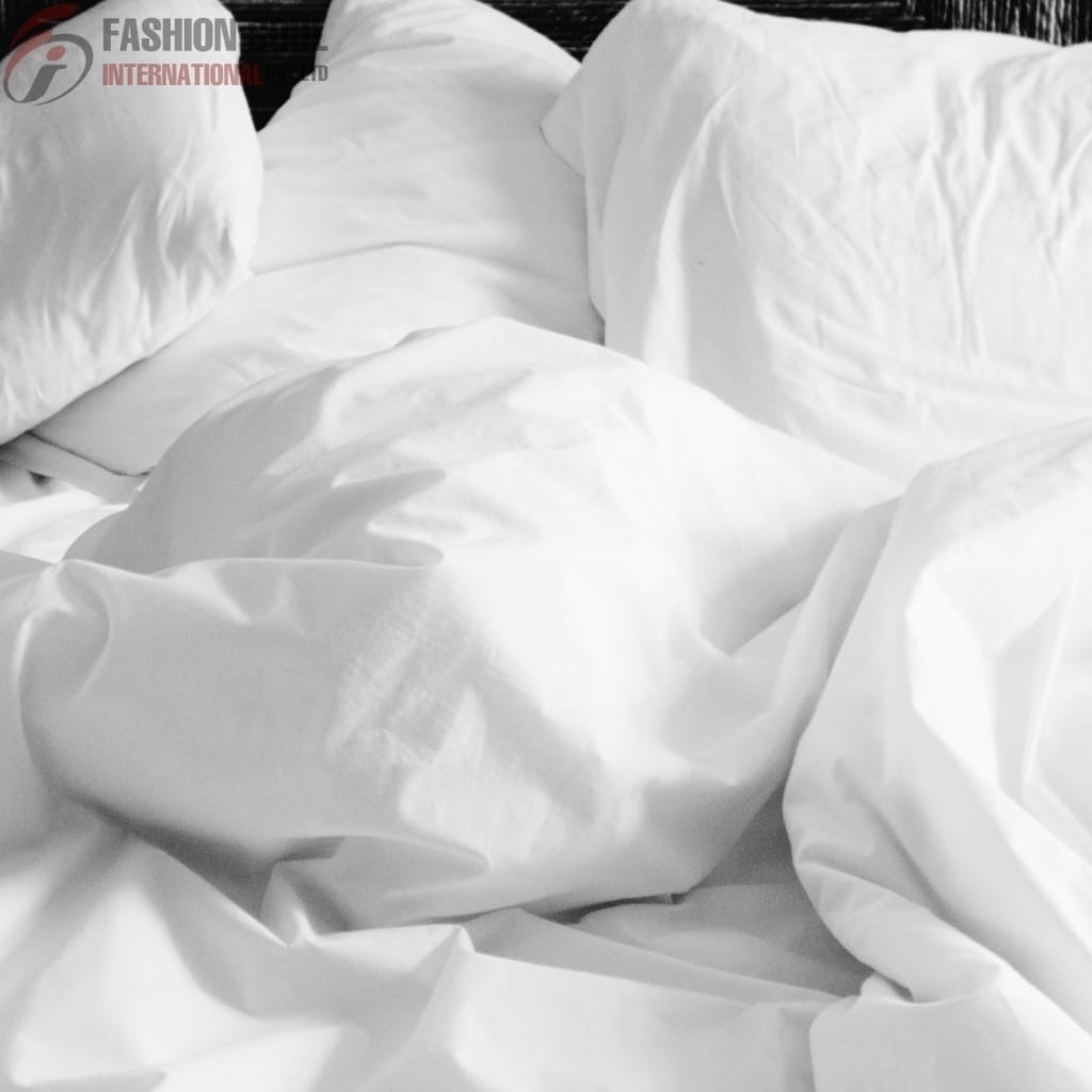 A close-up photograph of a bed with crumpled white bed linens and pillows, showcasing a slightly rumpled appearance.