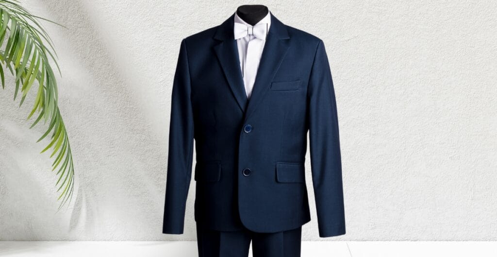 A classic navy sport coat displayed on a mannequin against a light textured wall, partially bordered by green foliage on the left side.