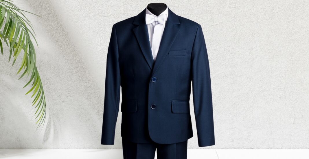 A classic navy sport coat displayed on a mannequin against a light textured wall, partially bordered by green foliage on the left side.