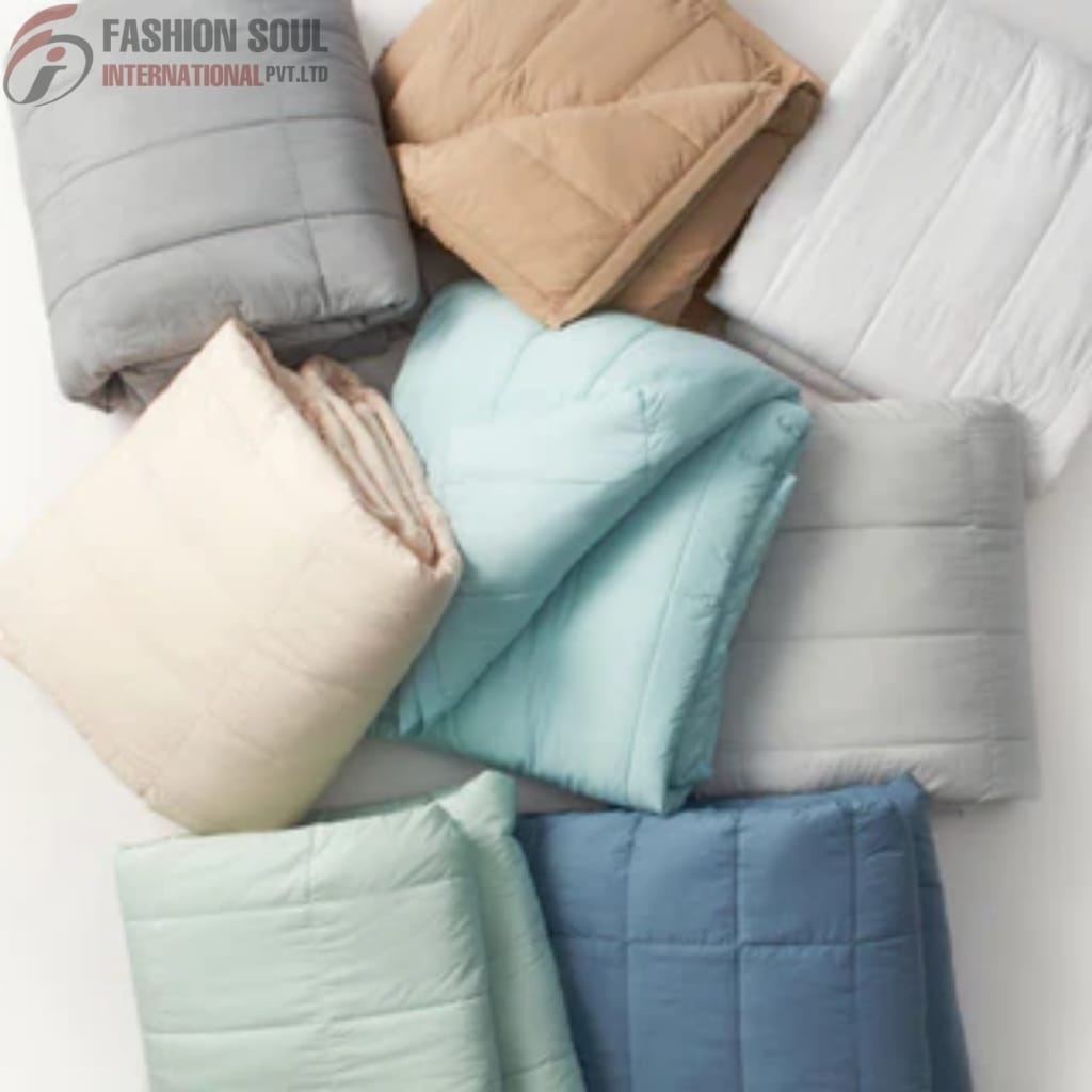 A collection of folded comforters and blankets in various pastel and neutral colors, arranged on a white surface.
