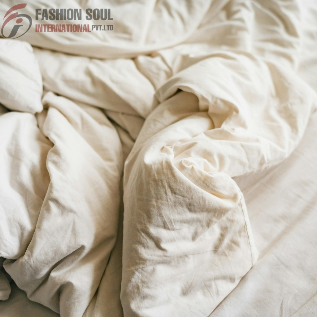 Cream-colored bed linen with a slightly wrinkled and rumpled appearance, partially folded and draped on a bed.