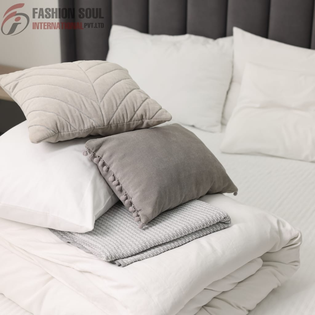 A neatly made bed with white pillows, a folded blanket, and two decorative pillows in shades of beige and gray, set against a dark upholstered headboard.