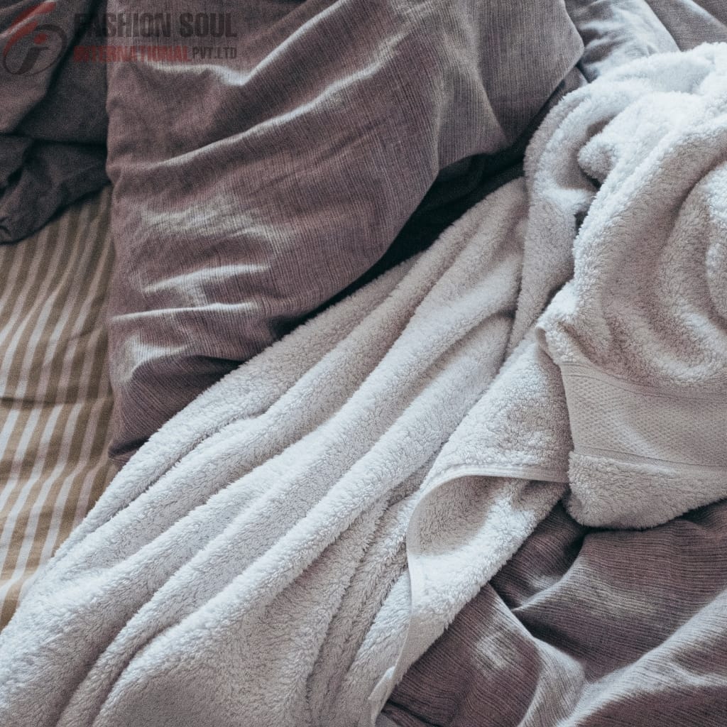 A cozy bed featuring a soft, white towel draped over a dark gray bedsheet, with a light gray pillow with black trim in the background.