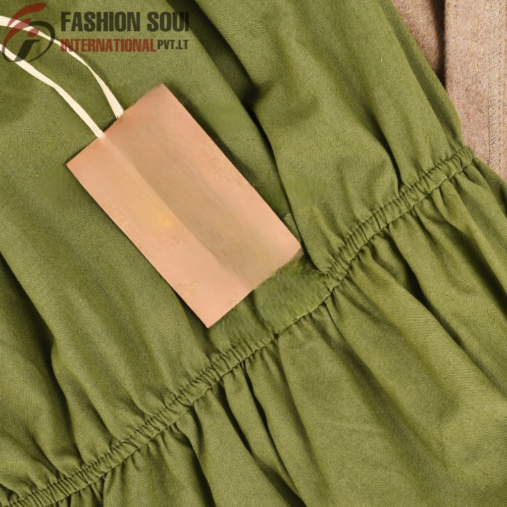 A close-up of a green fabric garment with a gathered elastic waistband, along with a blank beige tag attached by a white string.