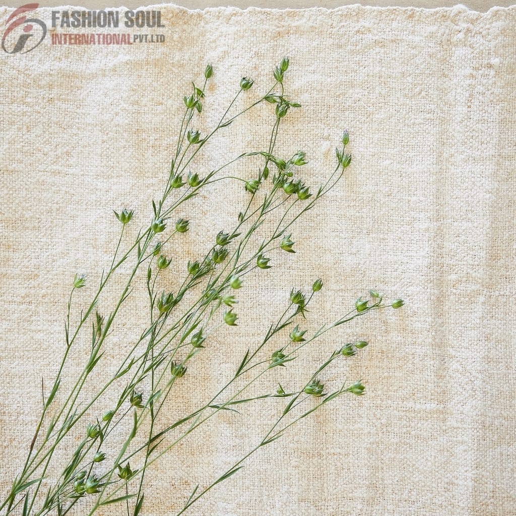 Close-up of delicate green plant stems with small buds, laid on a textured beige fabric background.