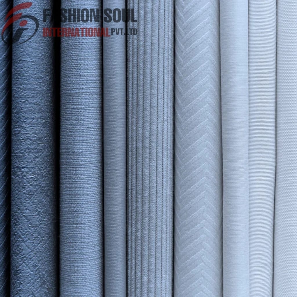 A row of eight neatly folded fabrics in shades of blue and grey, featuring various textures and patterns, with a watermark in the upper left corner reading